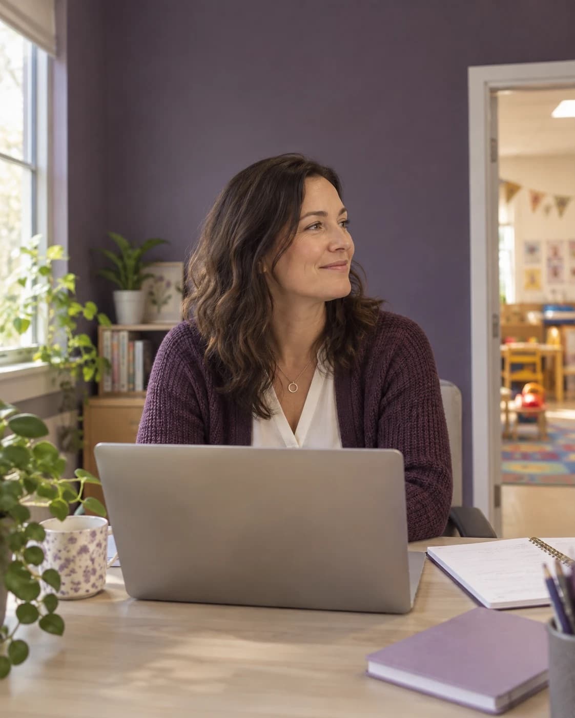 A childcare director at a desk in a plum-painted office, glancing toward the playroom